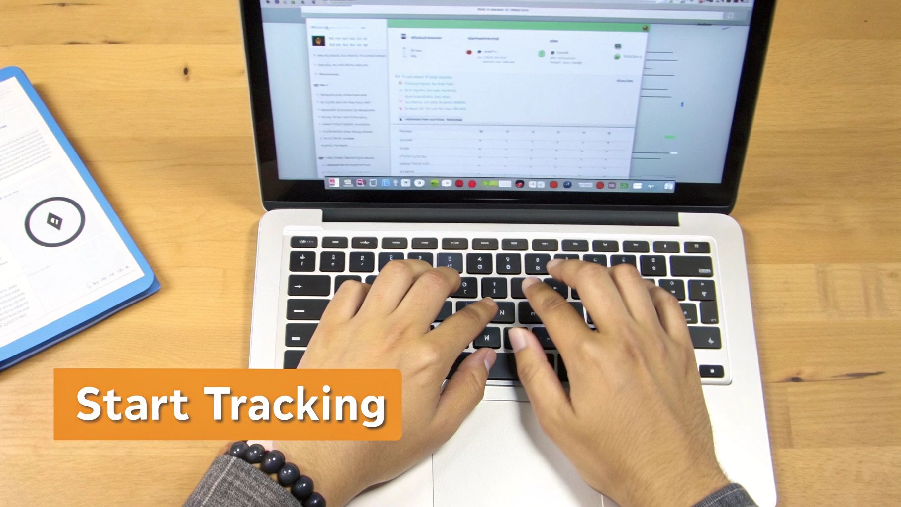Hands typing on a MacBook, displaying a time tracking application on a wooden desk.